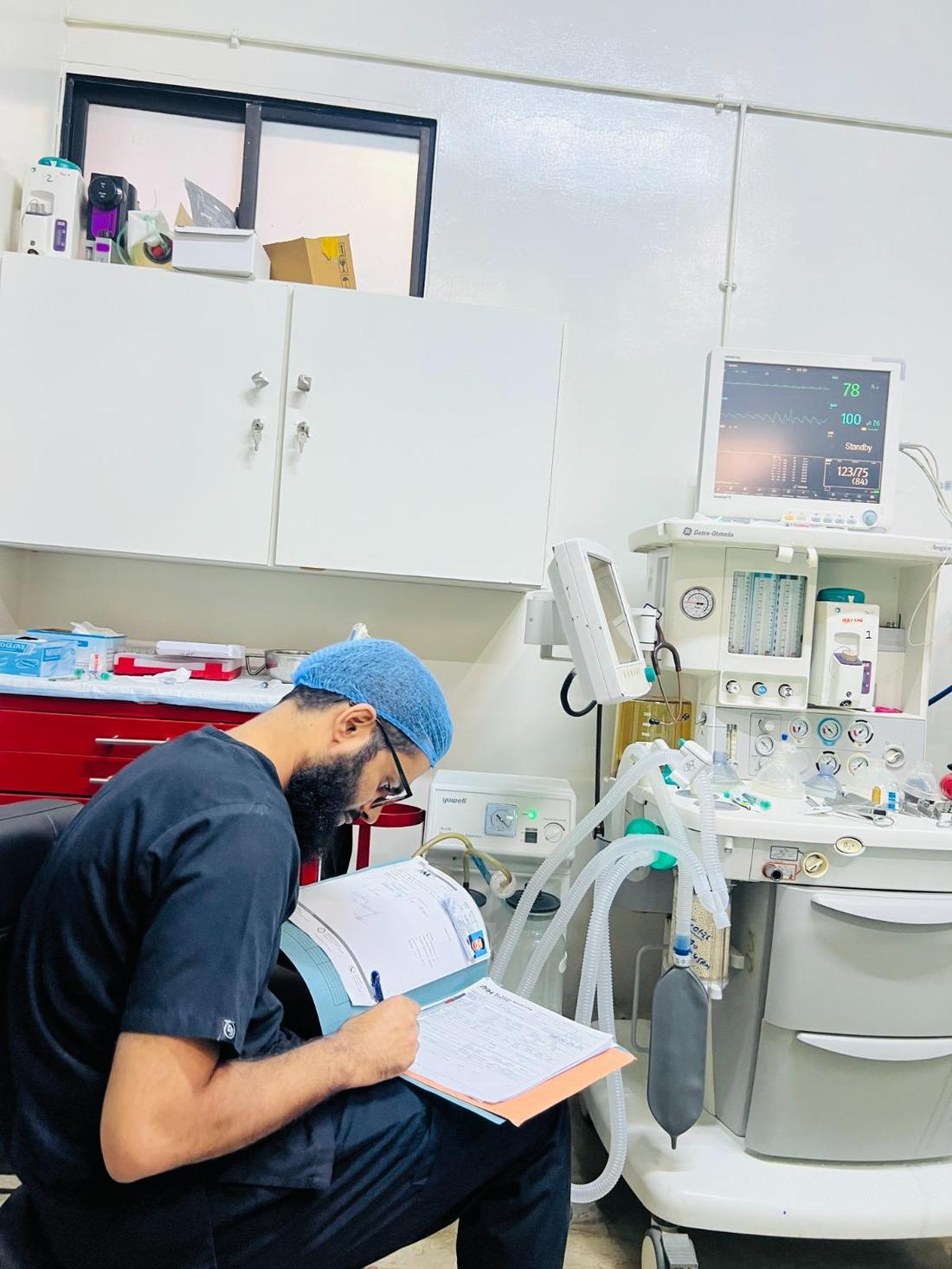 A doctor completes notes beside an anaesthesia machine